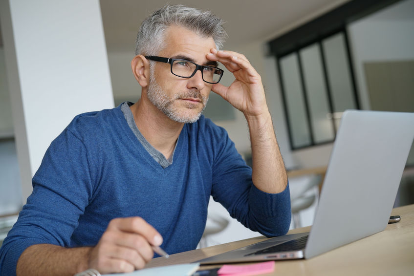 Middle-aged man working on laptop- thoughtful look