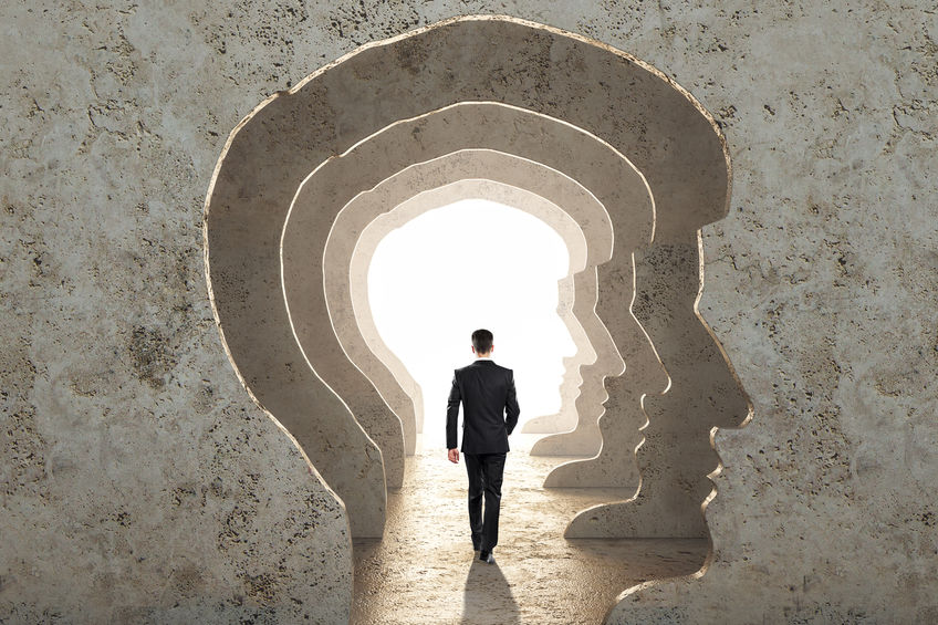 Back view of businessman walking in abstract concrete man head corridor with light. Abstraction and way concept.